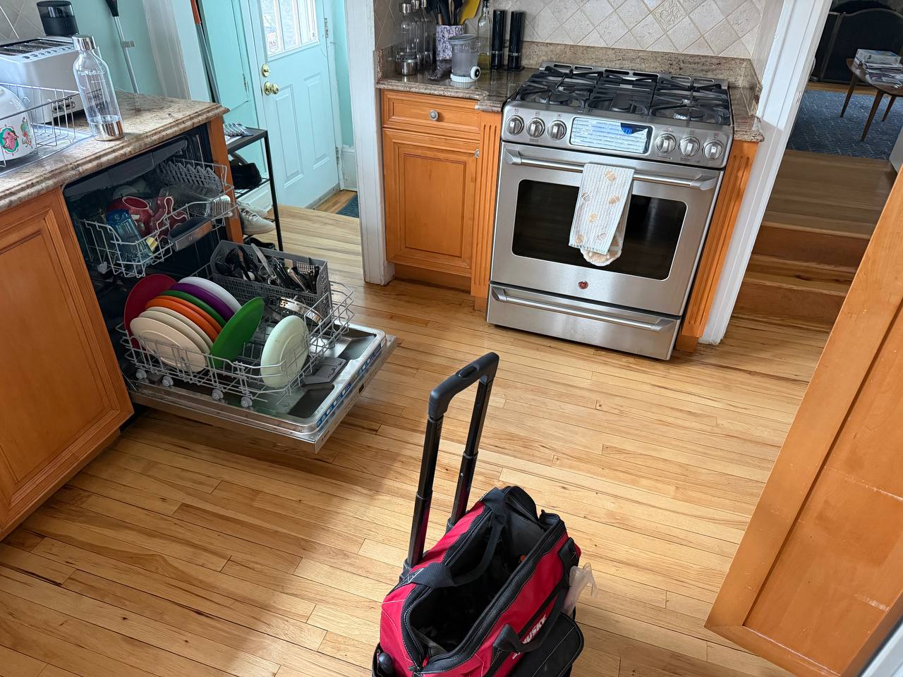 Open dishwasher loaded with dishes during a repair service call with technician tool bag on the kitchen floor