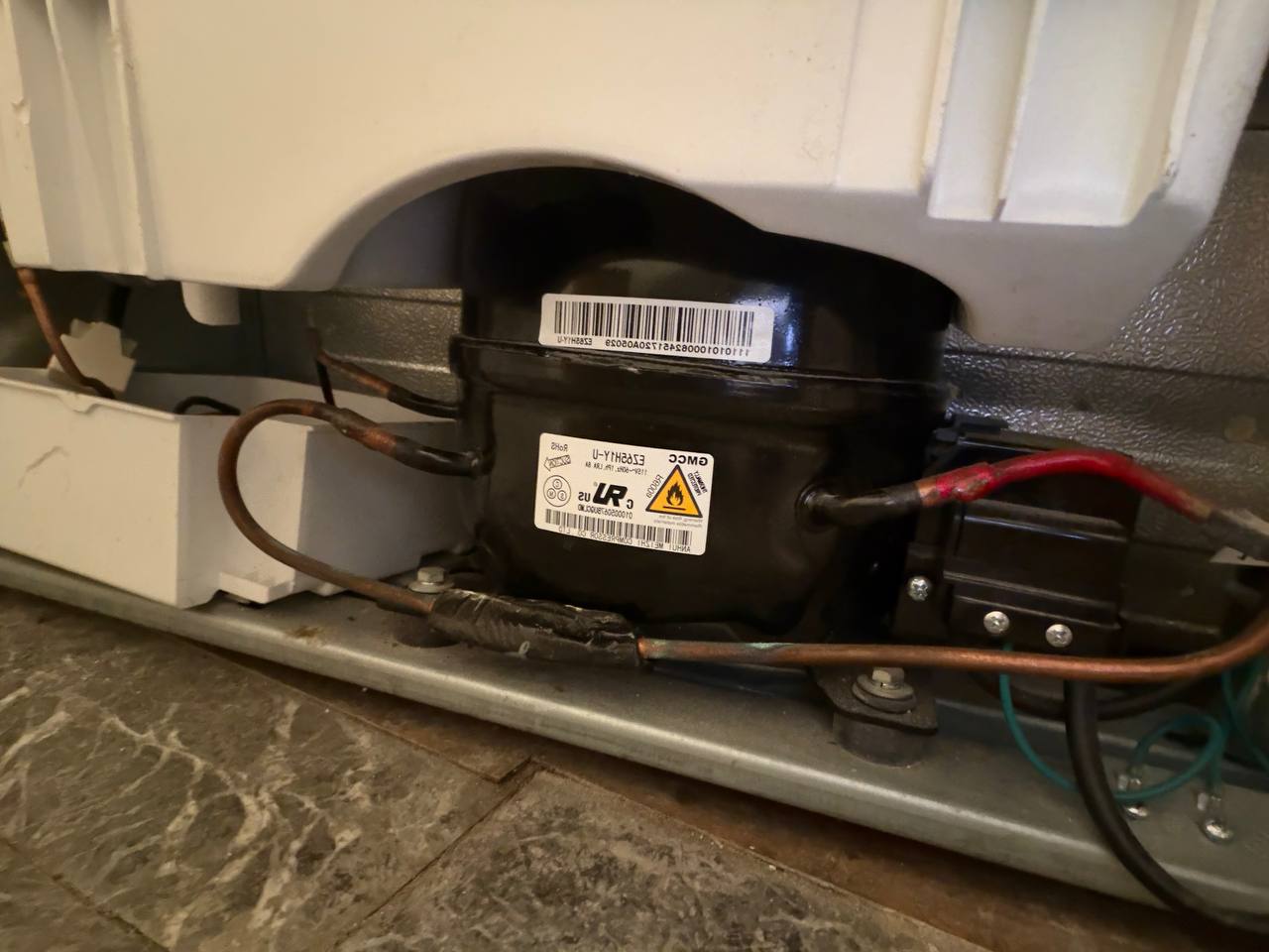 Technician repairing a refrigerator compressor with copper tubing and wiring during a service call in NYC